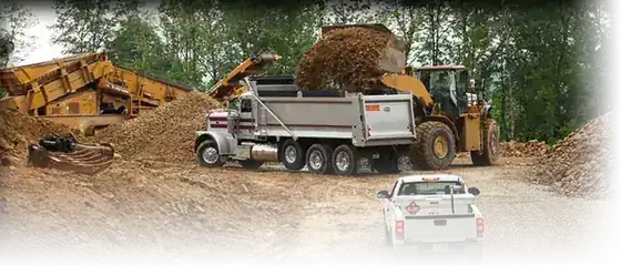 A red Shallenberger tri-axle dump truck at a screening plant