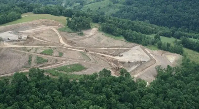 Aerial of a cleared and graded site cut into wooded hills