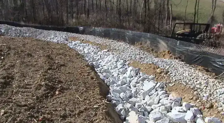 A riprap-lined drainage channel with silt fence on a graded slope