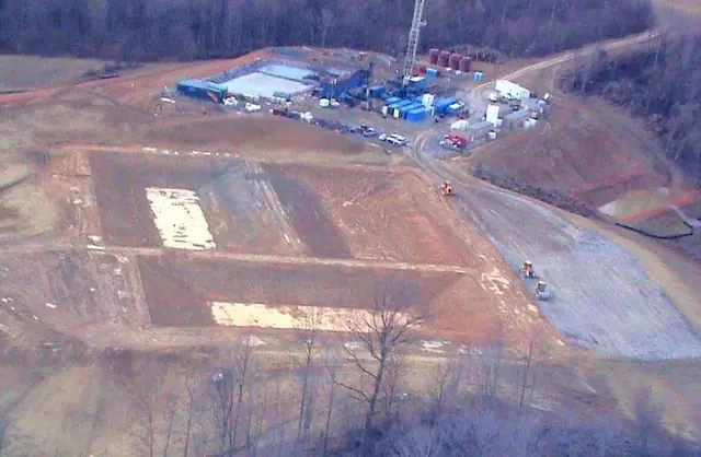 Aerial of graded well site pads with trailers and equipment at the far end
