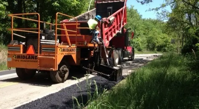 A paver working behind a red dump truck with the crew in hi-vis alongside