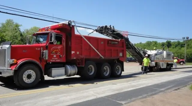 A red tri-axle dump truck and a milling machine under power lines